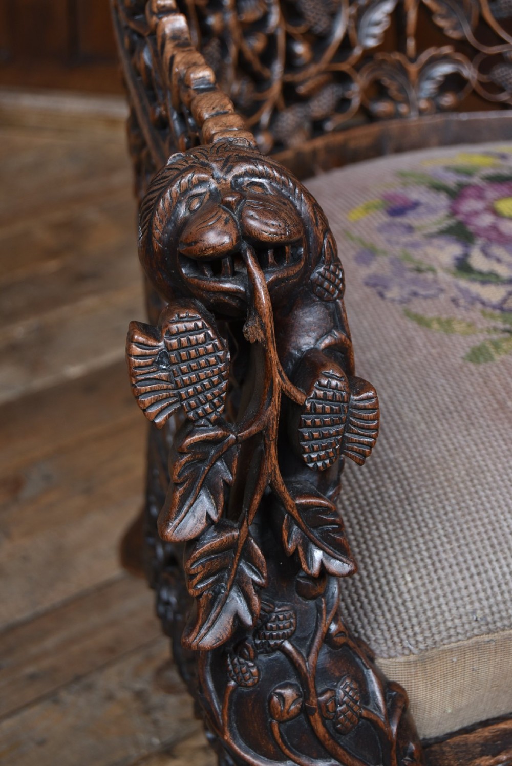 A nineteenth-century dark carved oak armchair featuring intricate openwork thistle motifs across the high arched back and sides, fitted with a floral needlepoint seat cushion. View II