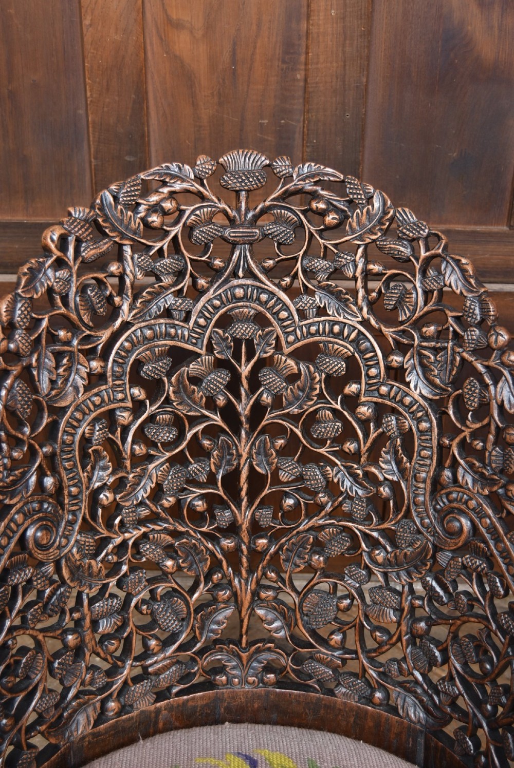 A nineteenth-century dark carved oak armchair featuring intricate openwork thistle motifs across the high arched back and sides, fitted with a floral needlepoint seat cushion. View V