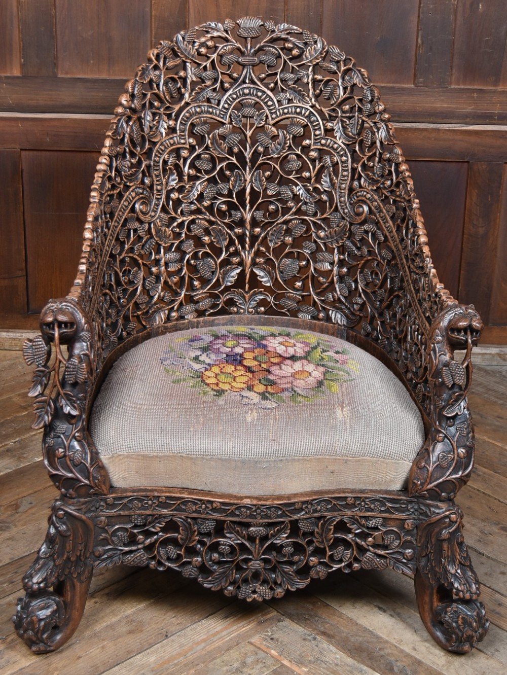 A nineteenth-century dark carved oak armchair featuring intricate openwork thistle motifs across the high arched back and sides, fitted with a floral needlepoint seat cushion. View VI