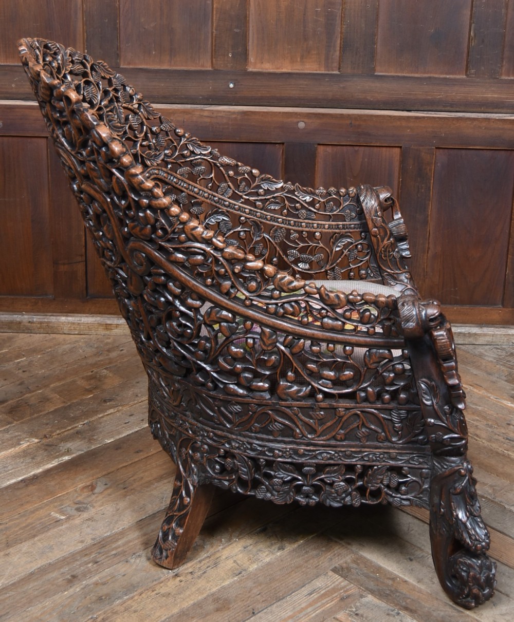 A nineteenth-century dark carved oak armchair featuring intricate openwork thistle motifs across the high arched back and sides, fitted with a floral needlepoint seat cushion. View IX