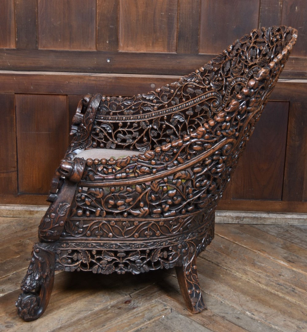 A nineteenth-century dark carved oak armchair featuring intricate openwork thistle motifs across the high arched back and sides, fitted with a floral needlepoint seat cushion. View XI