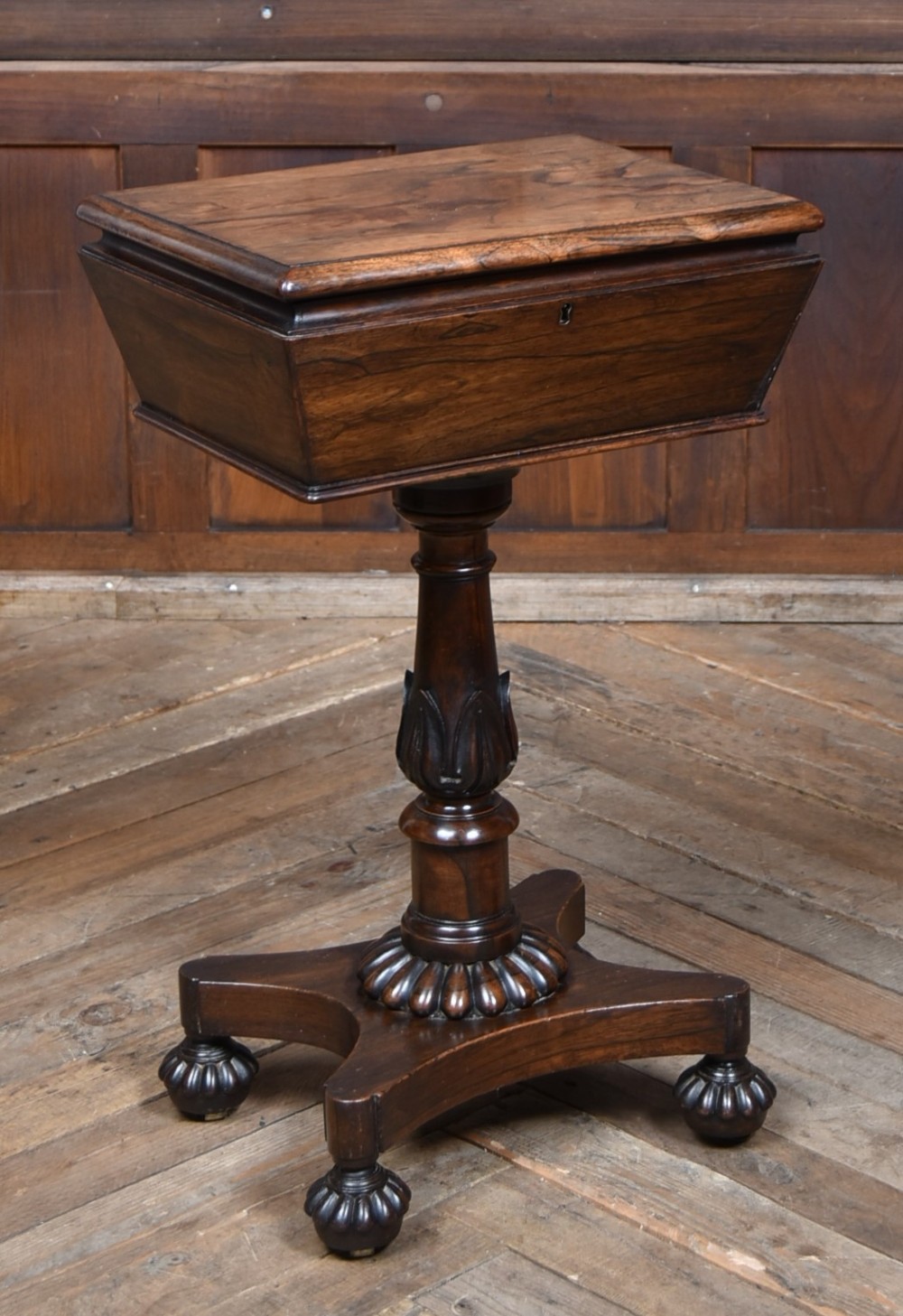 A Victorian dark rosewood teapoy featuring a sarcophagus-shaped chest top resting on a turned carved pedestal and quadruped base.