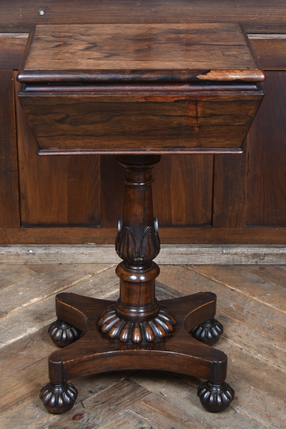 A Victorian dark rosewood teapoy featuring a sarcophagus-shaped chest top resting on a turned carved pedestal and quadruped base. View X