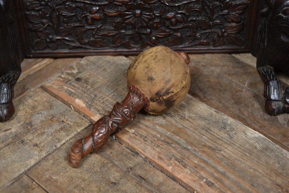 An intricately carved dark timber frame with foliage and figure details suspending a dark metal circular nipple gong. View XIV