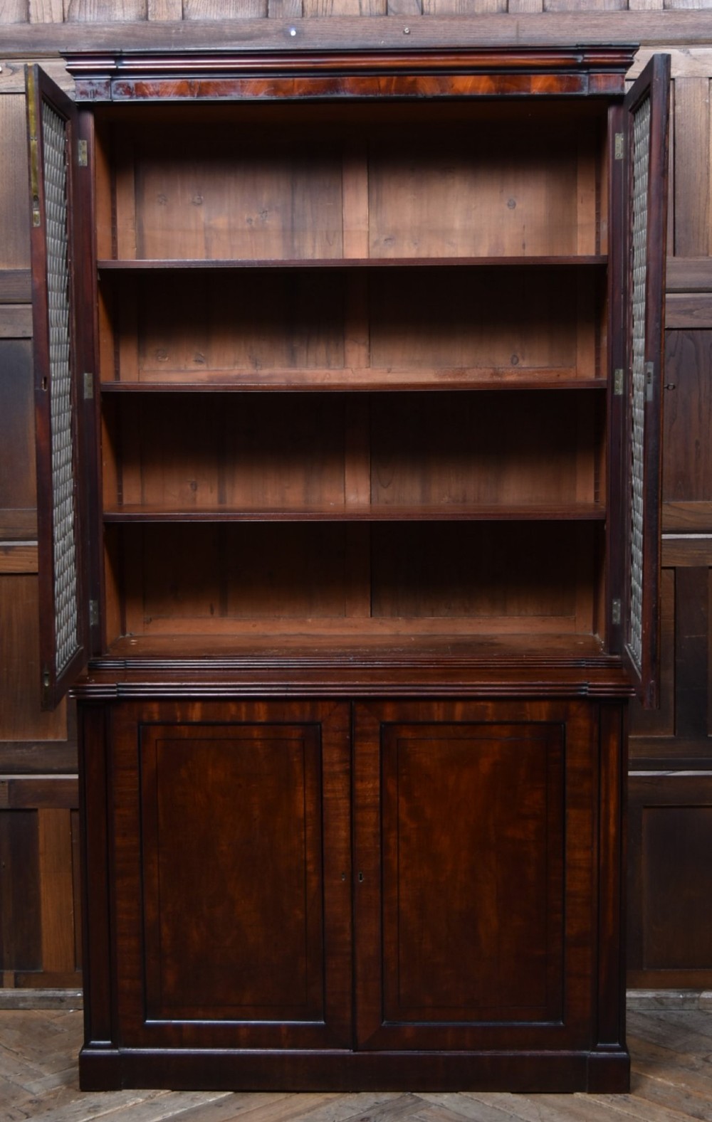 An antique two-part Georgian mahogany bookcase featuring double upper doors with diamond brass wire grilles over lower flame mahogany cupboard doors. View III