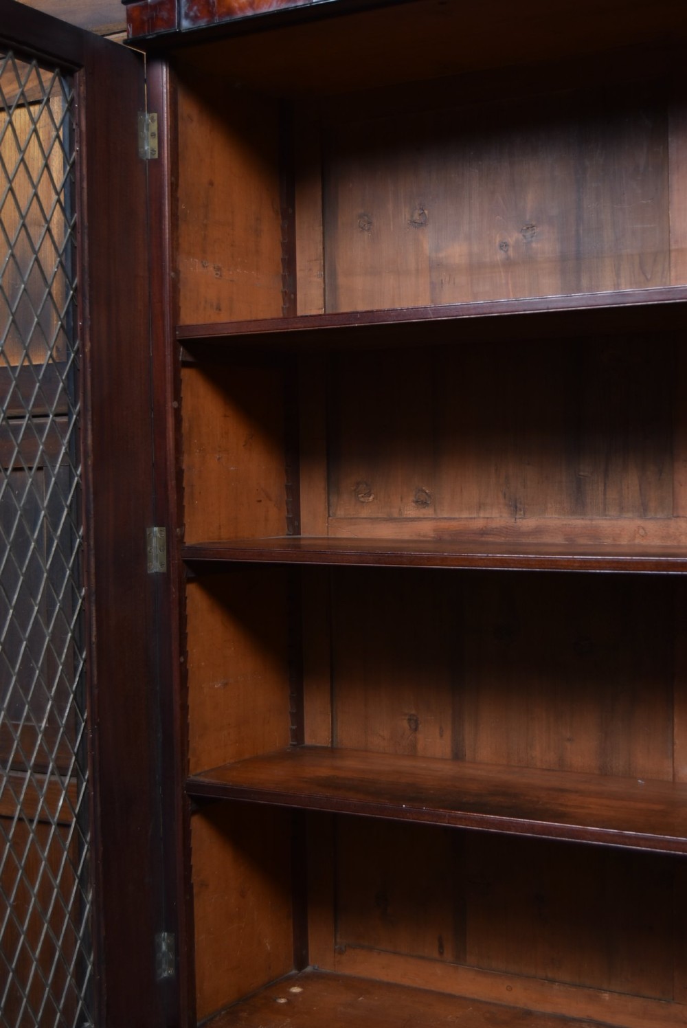 An antique two-part Georgian mahogany bookcase featuring double upper doors with diamond brass wire grilles over lower flame mahogany cupboard doors. View IV