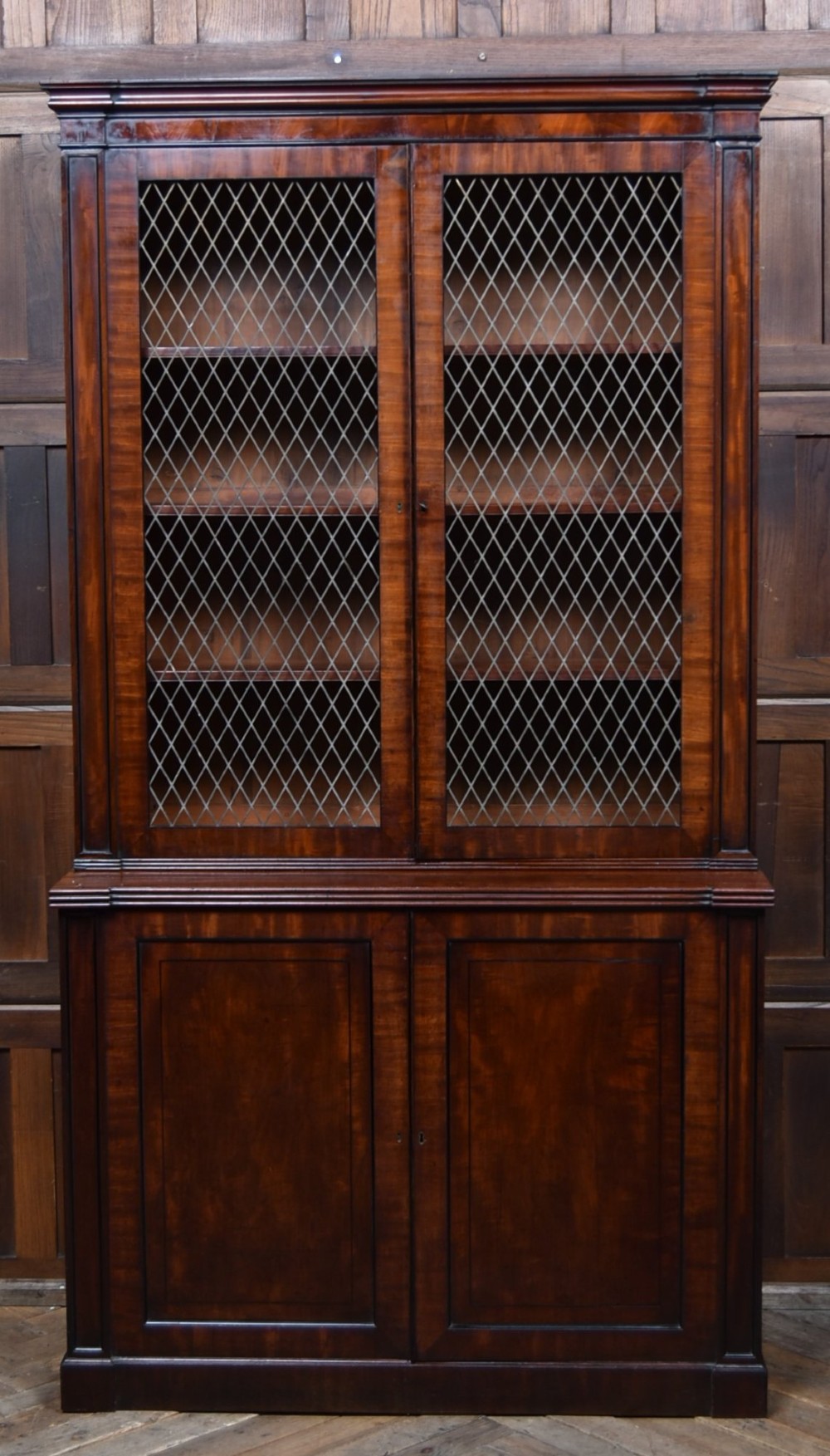 An antique two-part Georgian mahogany bookcase featuring double upper doors with diamond brass wire grilles over lower flame mahogany cupboard doors. View VI