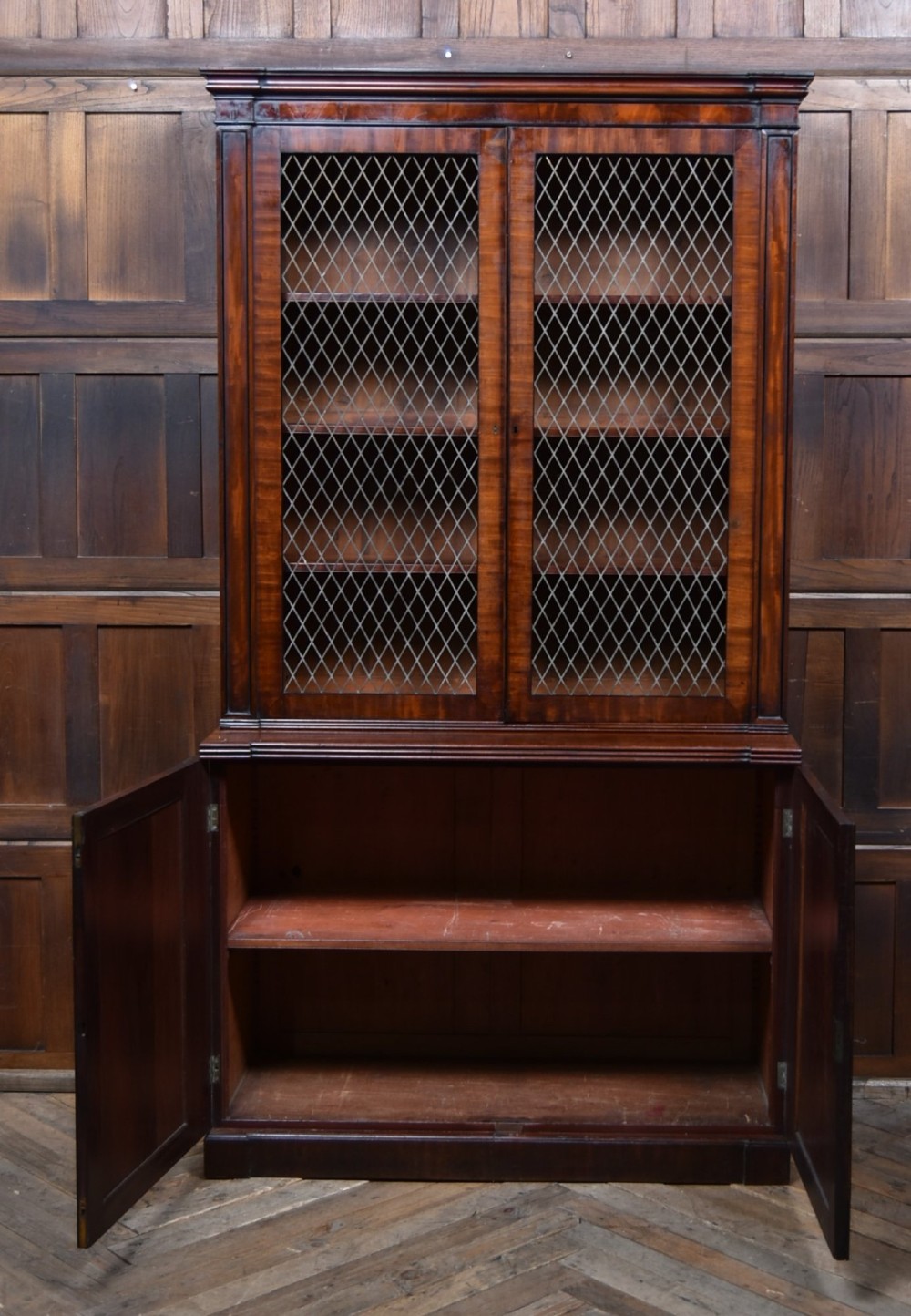 An antique two-part Georgian mahogany bookcase featuring double upper doors with diamond brass wire grilles over lower flame mahogany cupboard doors. View VII