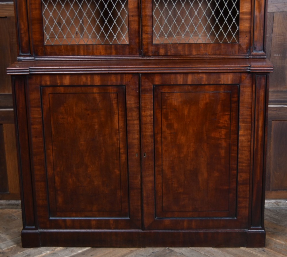 An antique two-part Georgian mahogany bookcase featuring double upper doors with diamond brass wire grilles over lower flame mahogany cupboard doors. View VIII