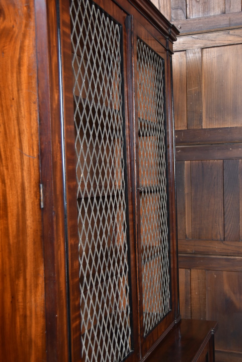 An antique two-part Georgian mahogany bookcase featuring double upper doors with diamond brass wire grilles over lower flame mahogany cupboard doors. View X