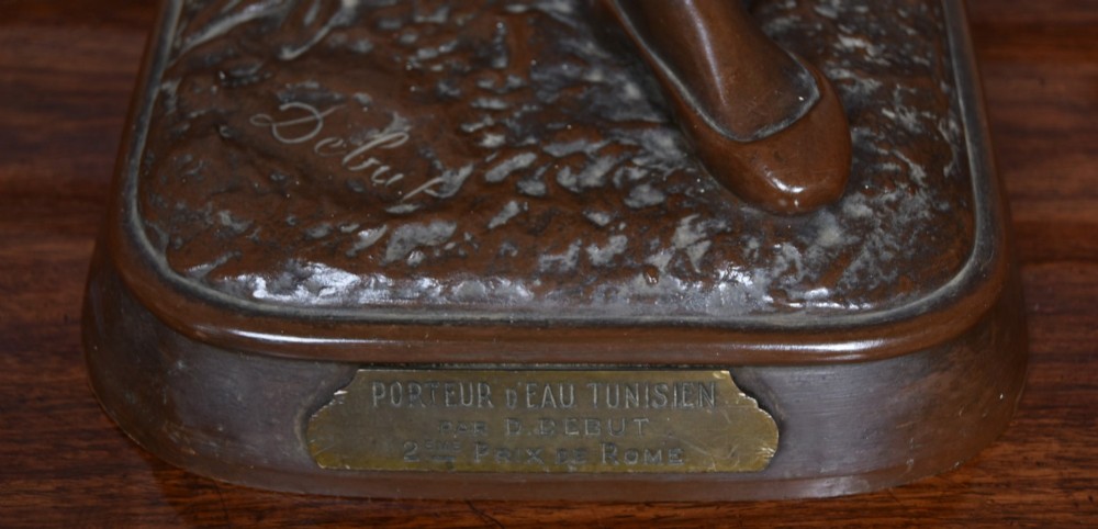A dark brown patinated bronze sculpture depicting a standing Tunisian water bearer carrying two vessels on a rectangular moulded base. View III