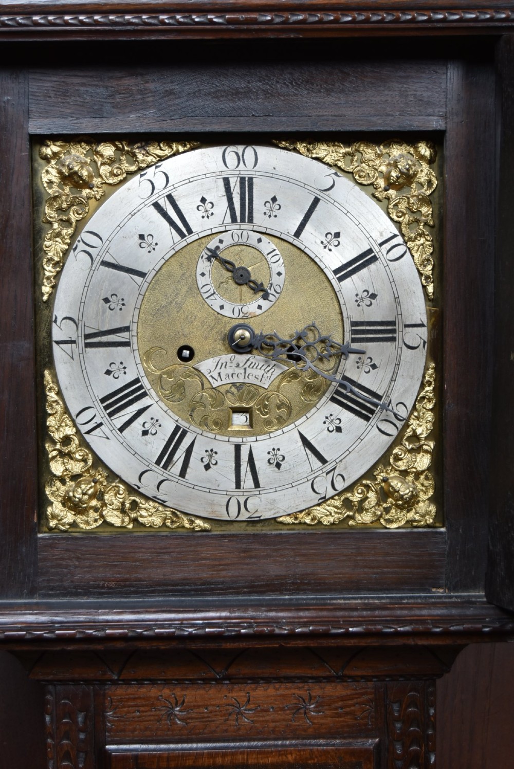 A tall carved dark oak longcase grandfather clock featuring intricate carved floral panels on the trunk and a brass dial signed John Smith Macclesfield. View III