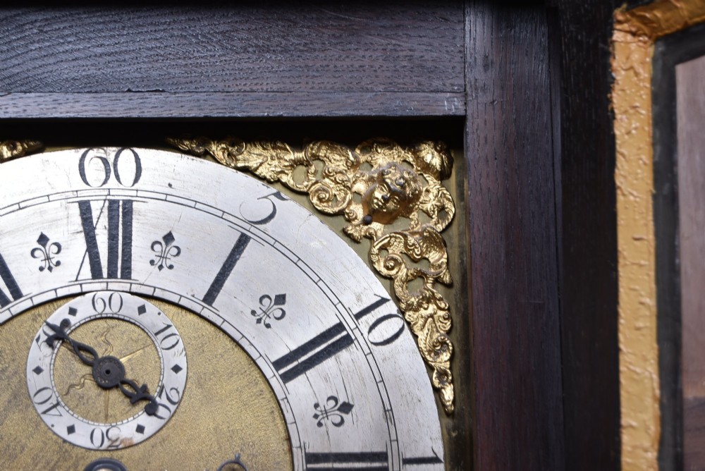 A tall carved dark oak longcase grandfather clock featuring intricate carved floral panels on the trunk and a brass dial signed John Smith Macclesfield. View IV
