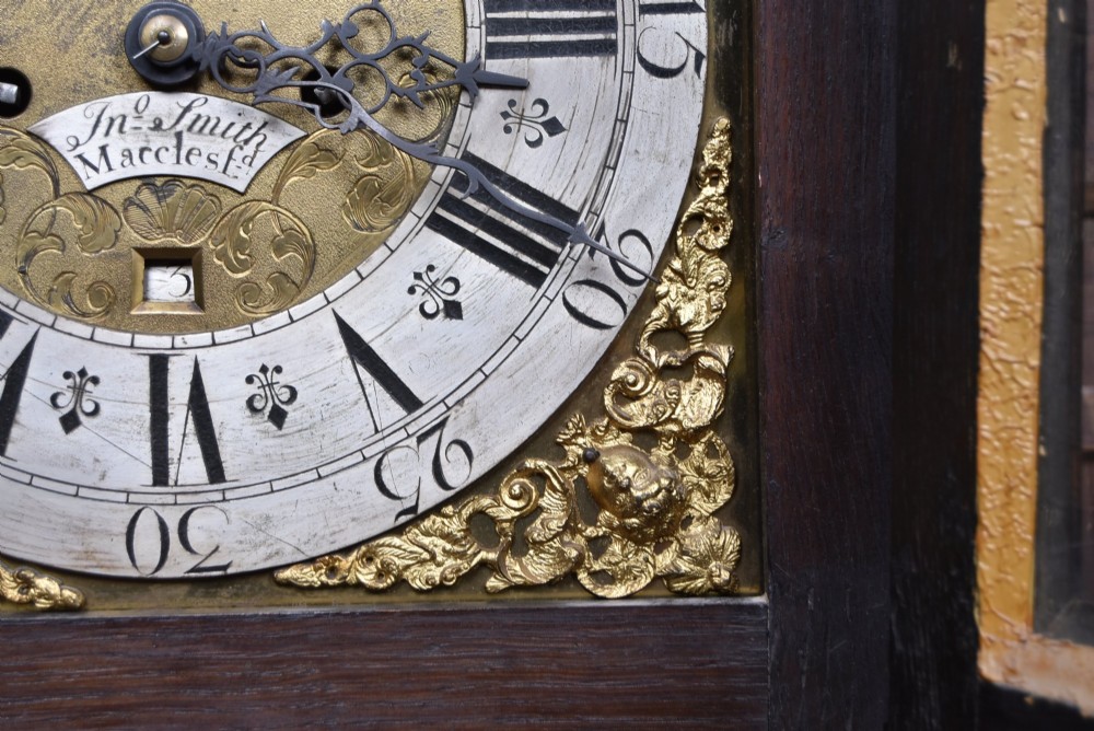 A tall carved dark oak longcase grandfather clock featuring intricate carved floral panels on the trunk and a brass dial signed John Smith Macclesfield. View V