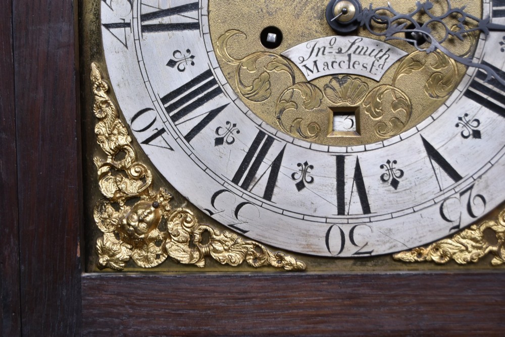 A tall carved dark oak longcase grandfather clock featuring intricate carved floral panels on the trunk and a brass dial signed John Smith Macclesfield. View VI