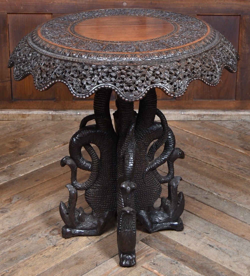 A 19th-century circular Burmese table in dark carved wood with a detailed openwork apron and a sculpted serpent base.