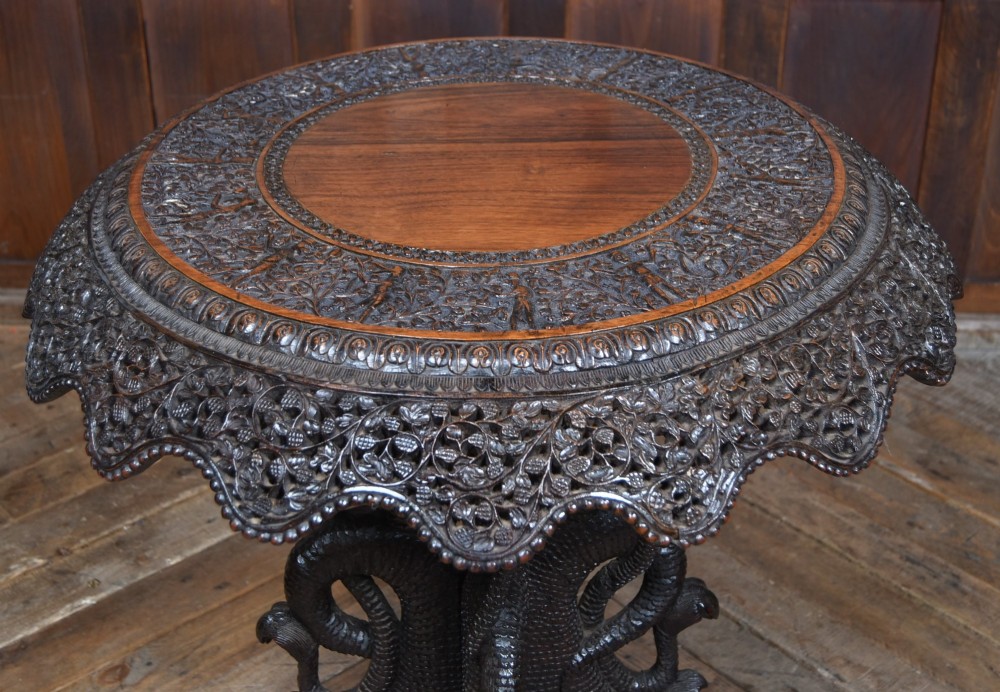 A 19th-century circular Burmese table in dark carved wood with a detailed openwork apron and a sculpted serpent base. View II
