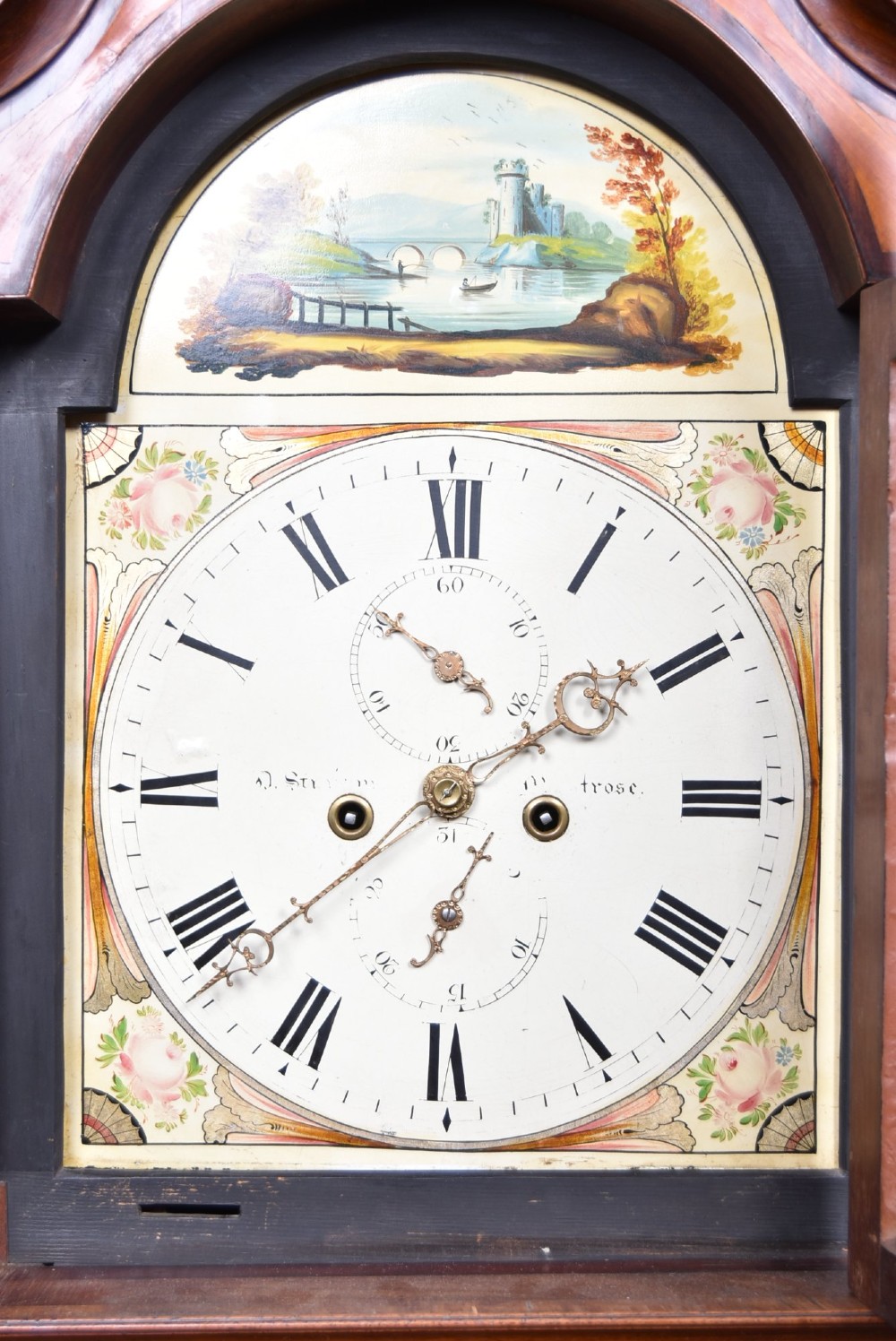 An antique Scottish flame mahogany longcase clock featuring a swan-neck pediment with brass finials and an arched painted dial. View IV