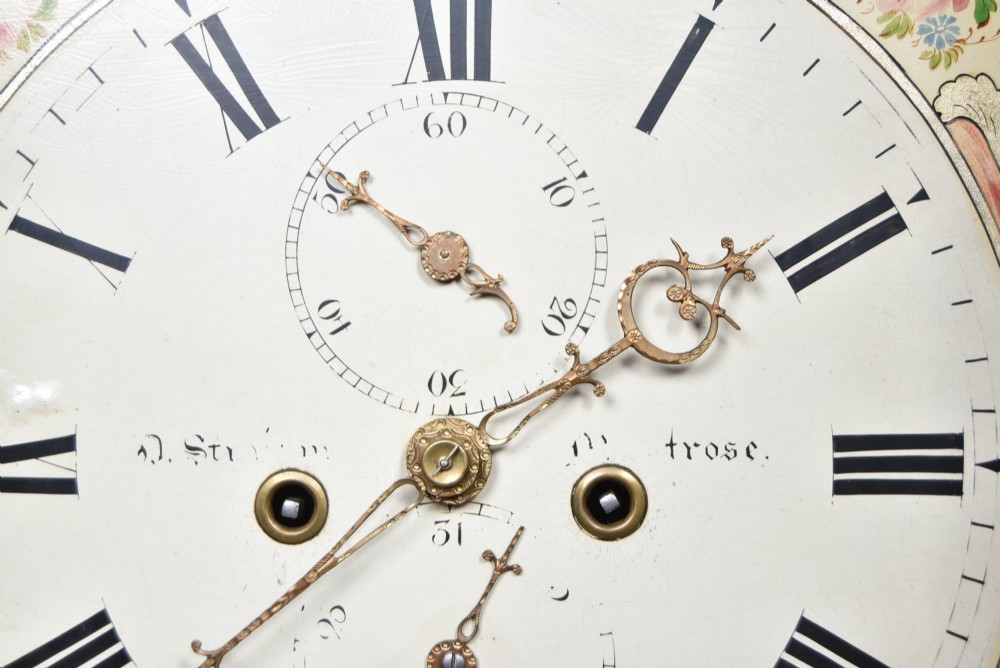 An antique Scottish flame mahogany longcase clock featuring a swan-neck pediment with brass finials and an arched painted dial. View V