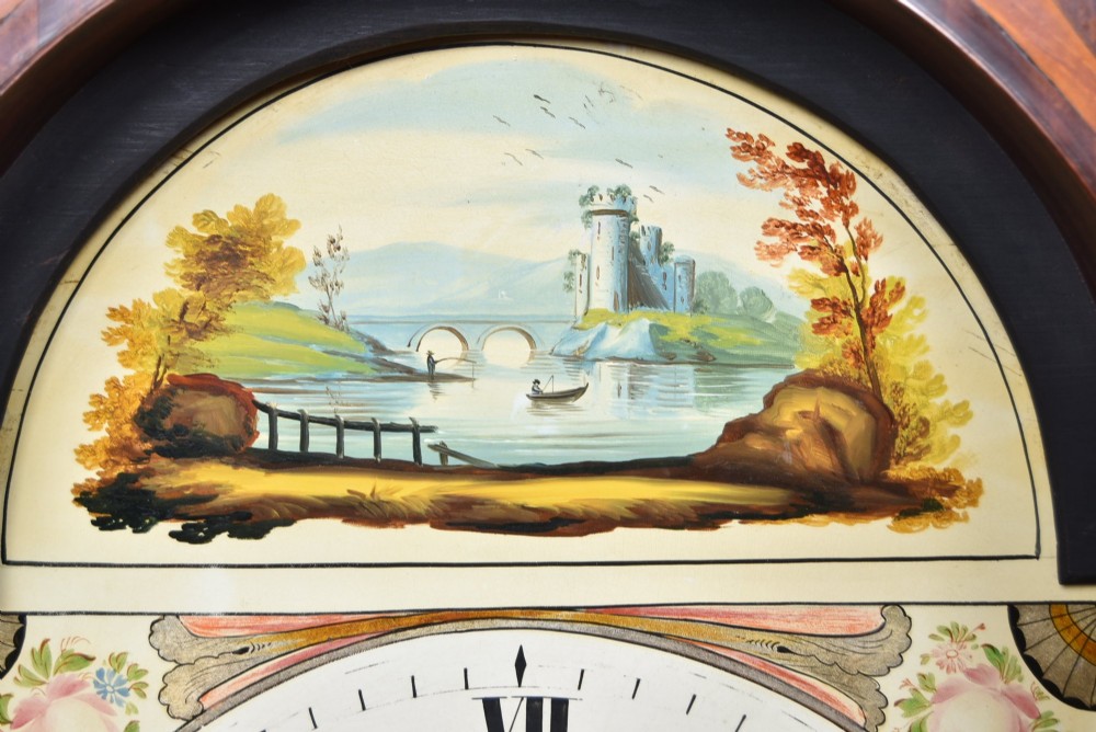 An antique Scottish flame mahogany longcase clock featuring a swan-neck pediment with brass finials and an arched painted dial. View VI