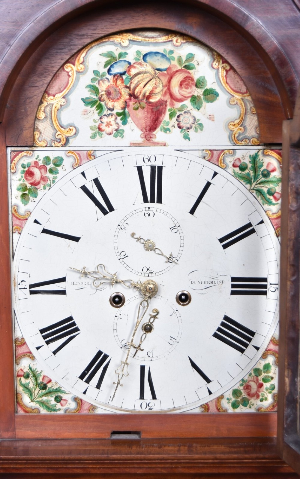 A Scottish mahogany longcase clock featuring a swan-neck pediment with brass finials, a hand-painted dial face, and flame mahogany veneers. View V