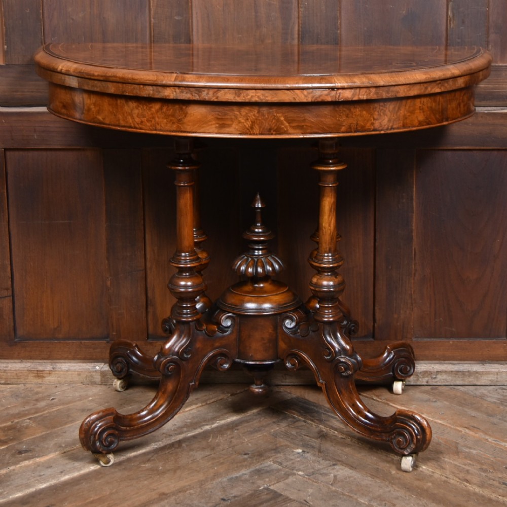 A Victorian burr walnut fold-over games table featuring a semi-circular top, dual turned column pedestal base, carved scroll legs, and ceramic castors. View II