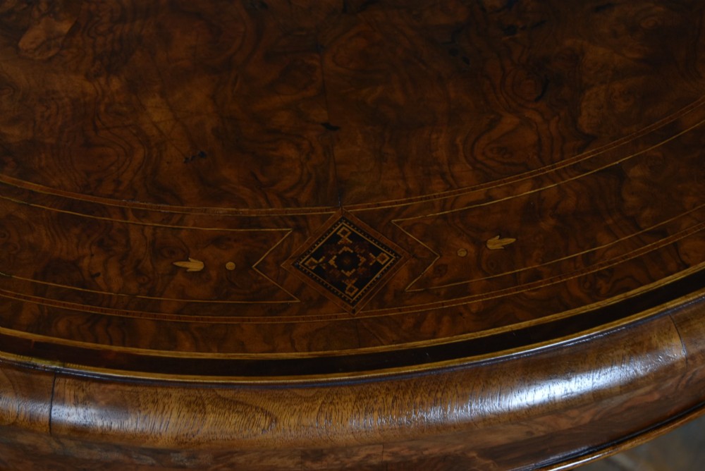 A Victorian burr walnut fold-over games table featuring a semi-circular top, dual turned column pedestal base, carved scroll legs, and ceramic castors. View V
