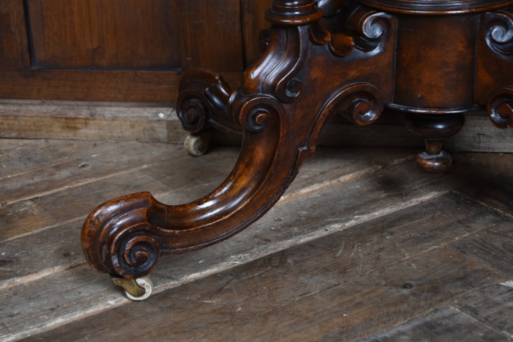 A Victorian burr walnut fold-over games table featuring a semi-circular top, dual turned column pedestal base, carved scroll legs, and ceramic castors. View VIII