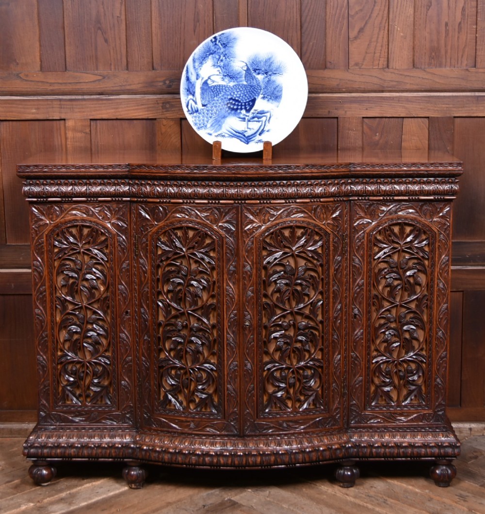 A nineteenth-century padouk wood sideboard featuring high-relief foliate hand-carving across four panelled cupboard doors and a breakfront profile.