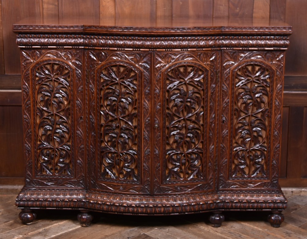 A nineteenth-century padouk wood sideboard featuring high-relief foliate hand-carving across four panelled cupboard doors and a breakfront profile. View II