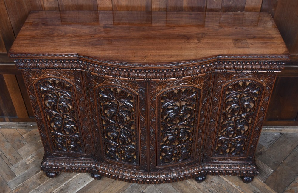 A nineteenth-century padouk wood sideboard featuring high-relief foliate hand-carving across four panelled cupboard doors and a breakfront profile. View III