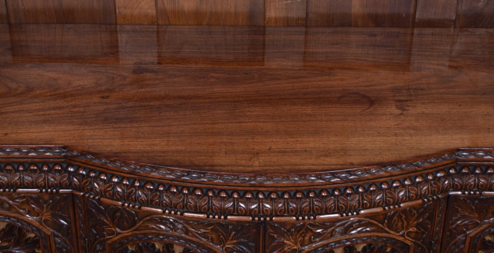 A nineteenth-century padouk wood sideboard featuring high-relief foliate hand-carving across four panelled cupboard doors and a breakfront profile. View V