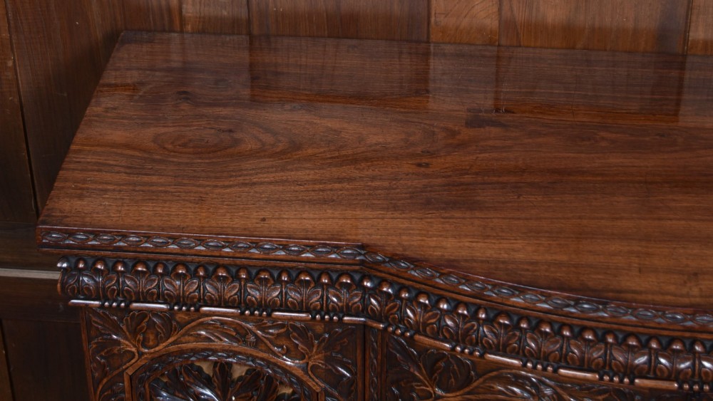 A nineteenth-century padouk wood sideboard featuring high-relief foliate hand-carving across four panelled cupboard doors and a breakfront profile. View VI