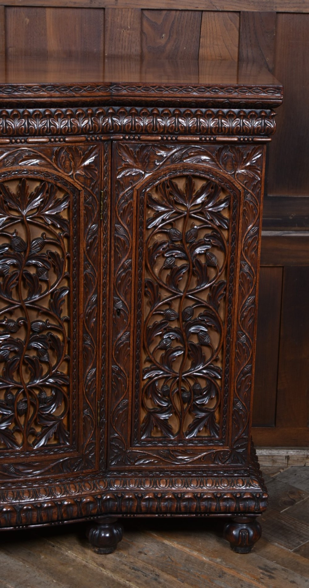 A nineteenth-century padouk wood sideboard featuring high-relief foliate hand-carving across four panelled cupboard doors and a breakfront profile. View VII