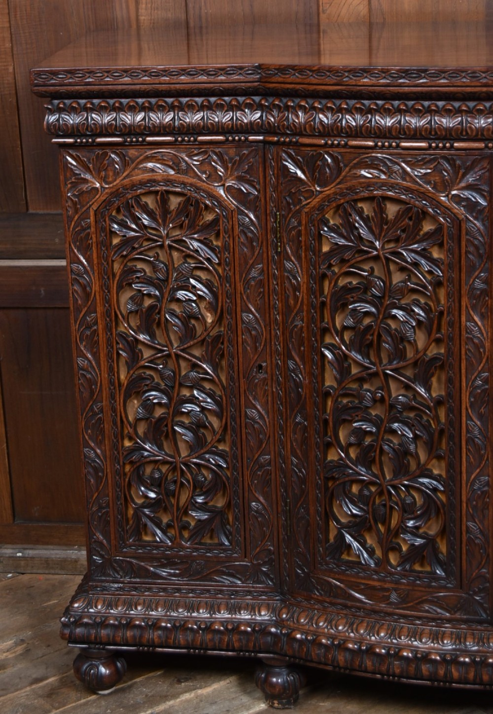 A nineteenth-century padouk wood sideboard featuring high-relief foliate hand-carving across four panelled cupboard doors and a breakfront profile. View VIII