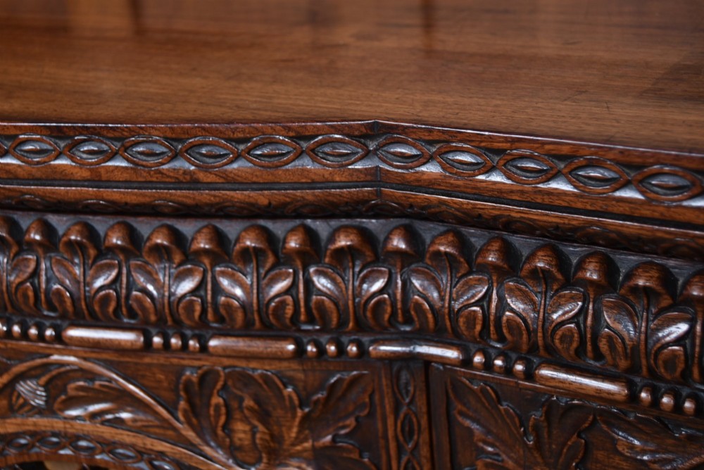 A nineteenth-century padouk wood sideboard featuring high-relief foliate hand-carving across four panelled cupboard doors and a breakfront profile. View IX