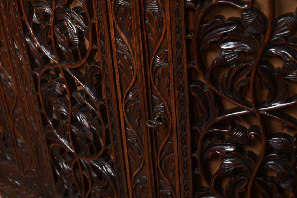 A nineteenth-century padouk wood sideboard featuring high-relief foliate hand-carving across four panelled cupboard doors and a breakfront profile. View X