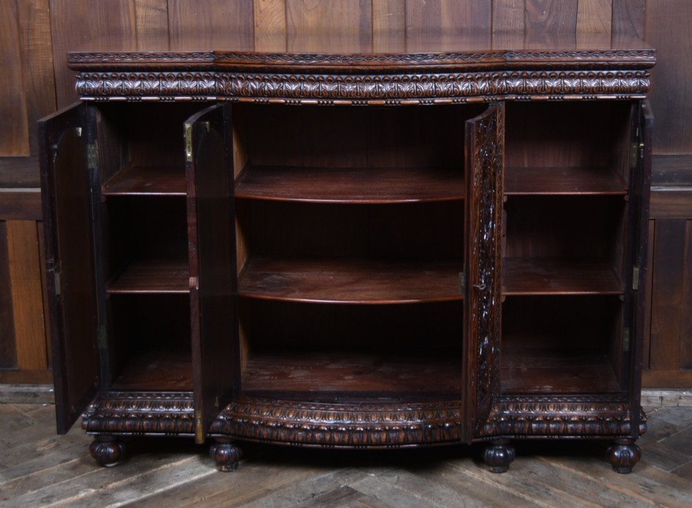A nineteenth-century padouk wood sideboard featuring high-relief foliate hand-carving across four panelled cupboard doors and a breakfront profile. View XI