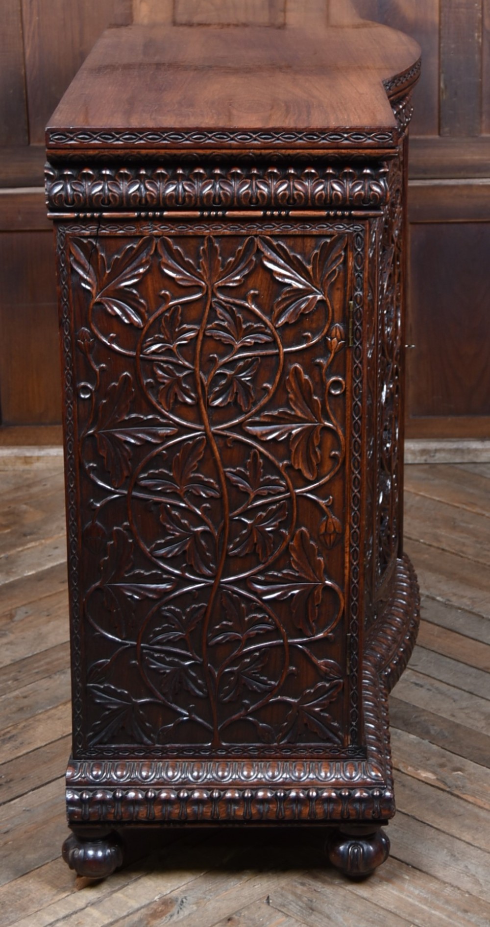 A nineteenth-century padouk wood sideboard featuring high-relief foliate hand-carving across four panelled cupboard doors and a breakfront profile. View XIII