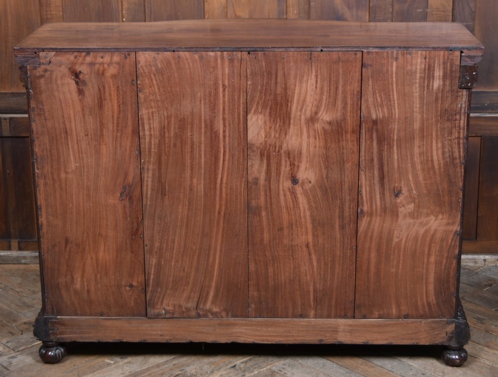 A nineteenth-century padouk wood sideboard featuring high-relief foliate hand-carving across four panelled cupboard doors and a breakfront profile. View XIV