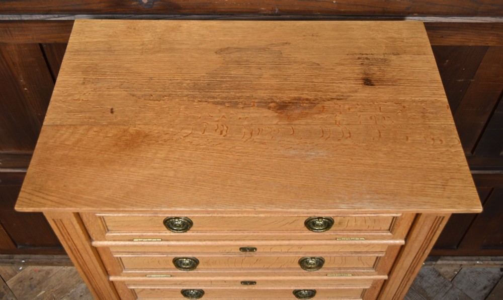 An Edwardian light oak filing cabinet with five stacked fall-front drawers featuring brass ring pulls, supported on square legs with a lower open shelf. View III