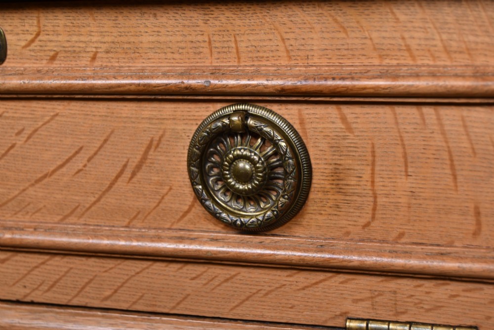 An Edwardian light oak filing cabinet with five stacked fall-front drawers featuring brass ring pulls, supported on square legs with a lower open shelf. View IV