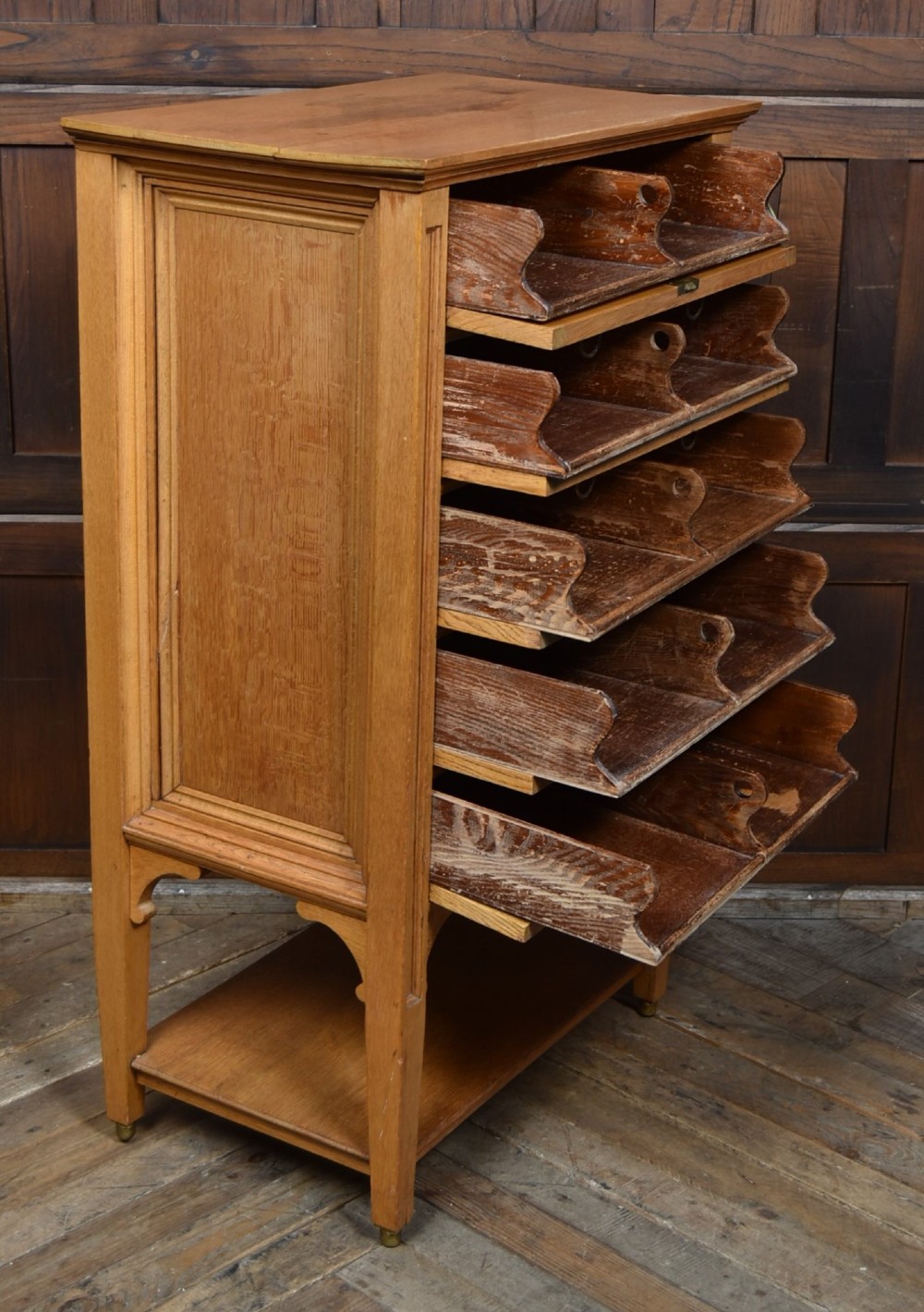 An Edwardian light oak filing cabinet with five stacked fall-front drawers featuring brass ring pulls, supported on square legs with a lower open shelf. View VII