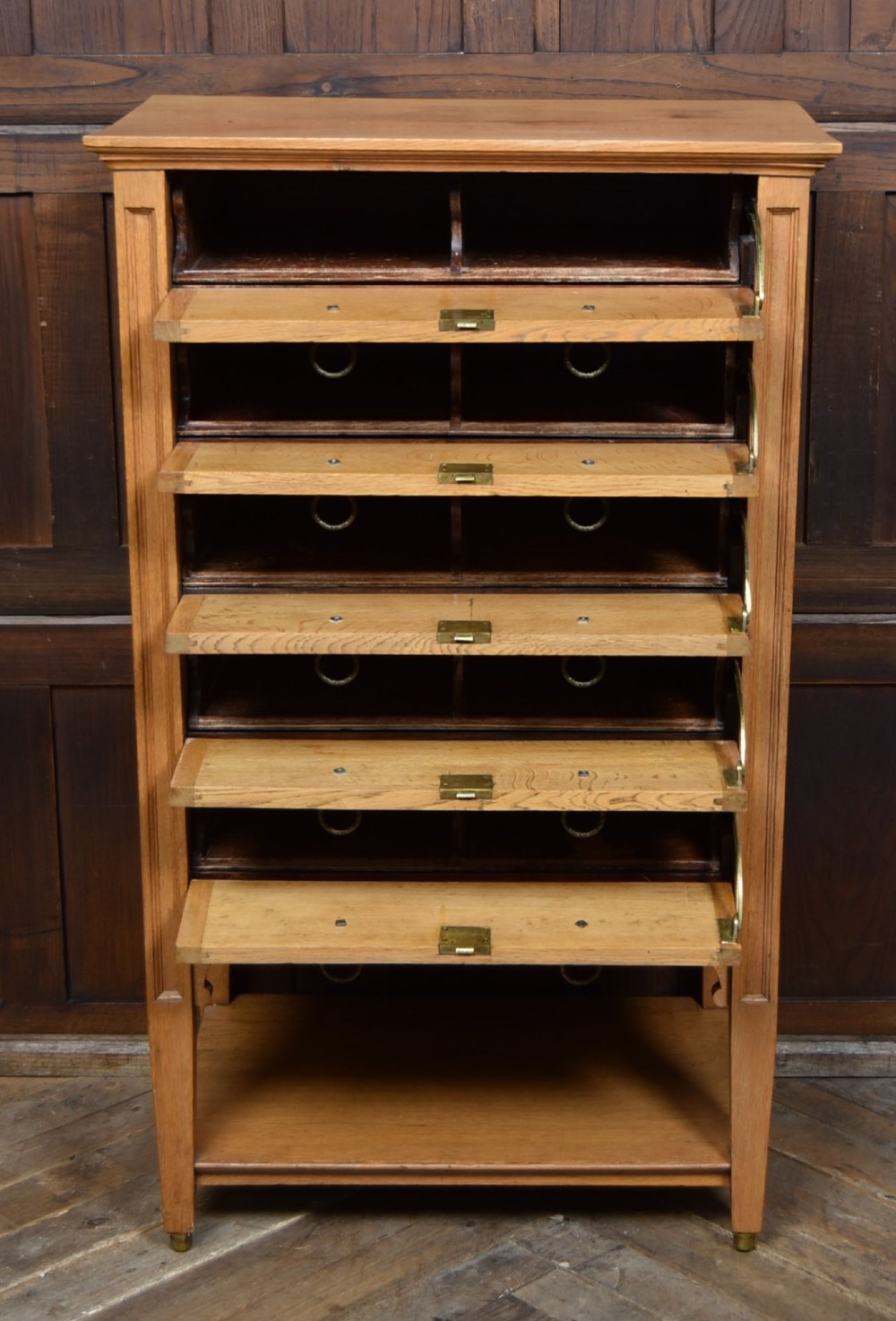 An Edwardian light oak filing cabinet with five stacked fall-front drawers featuring brass ring pulls, supported on square legs with a lower open shelf. View IX