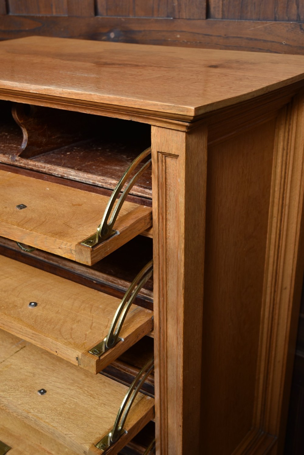 An Edwardian light oak filing cabinet with five stacked fall-front drawers featuring brass ring pulls, supported on square legs with a lower open shelf. View X