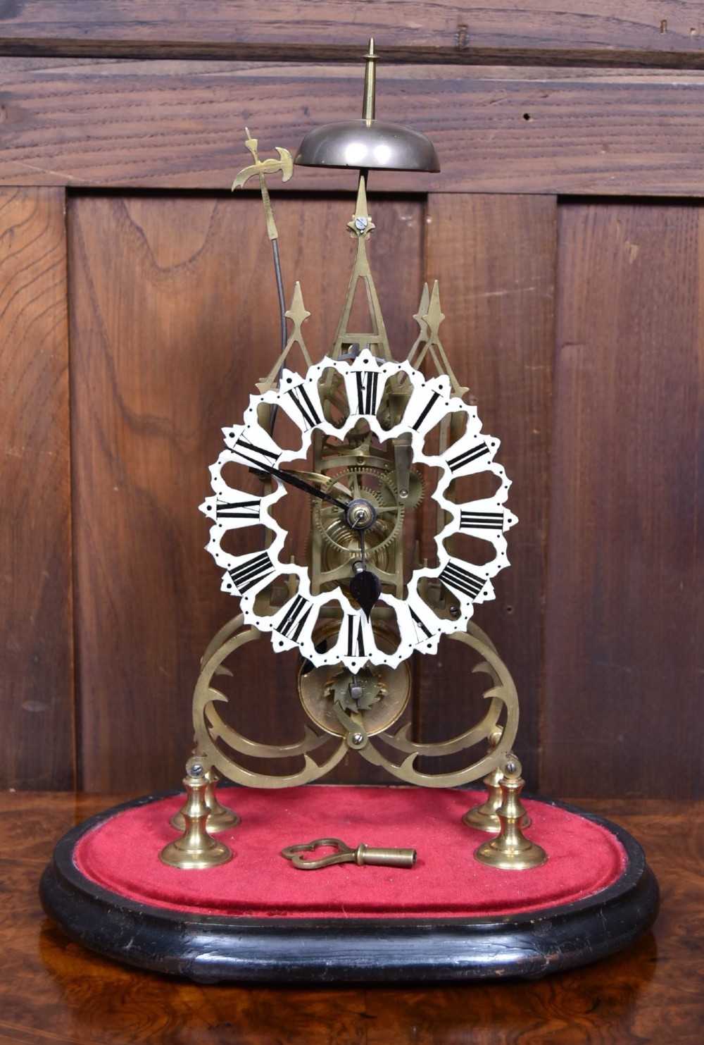 A Victorian brass skeleton clock with an openwork pierced dial and top bell, enclosed within a glass dome on an ebonised wooden base. View II