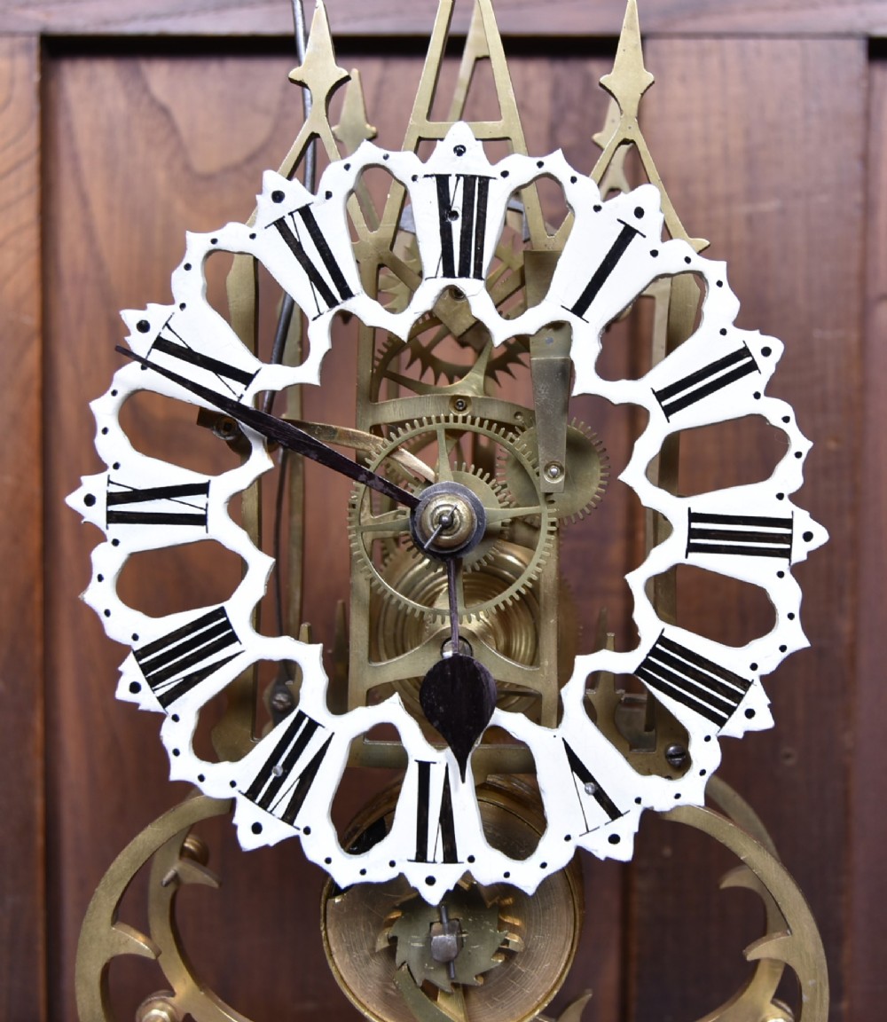A Victorian brass skeleton clock with an openwork pierced dial and top bell, enclosed within a glass dome on an ebonised wooden base. View III
