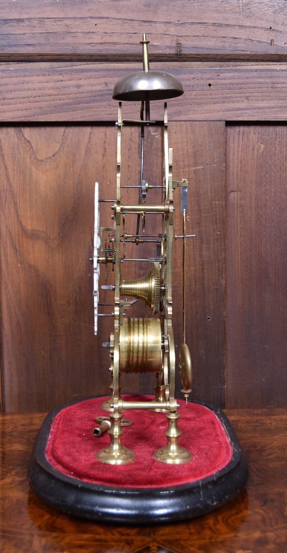 A Victorian brass skeleton clock with an openwork pierced dial and top bell, enclosed within a glass dome on an ebonised wooden base. View IV