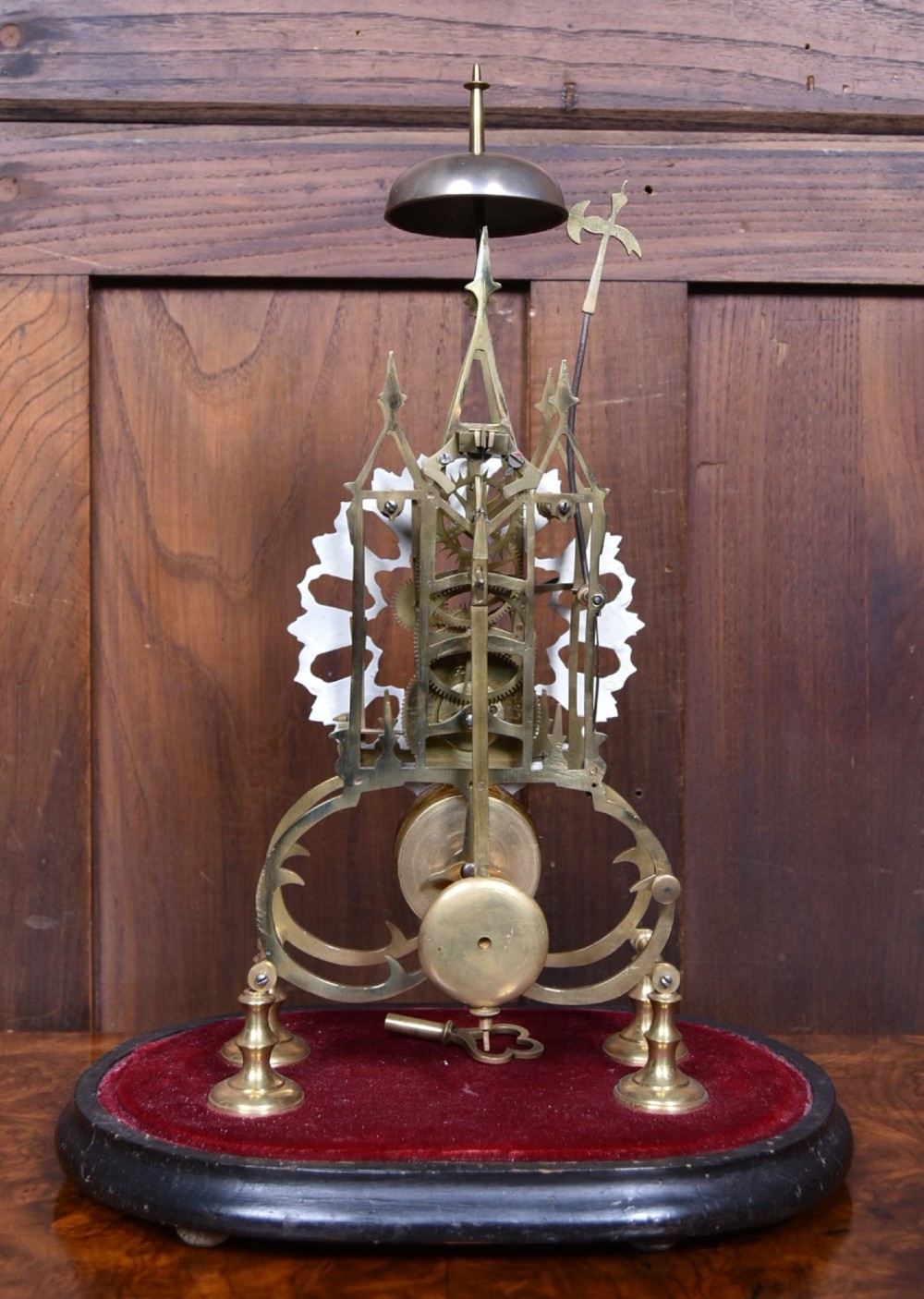 A Victorian brass skeleton clock with an openwork pierced dial and top bell, enclosed within a glass dome on an ebonised wooden base. View V