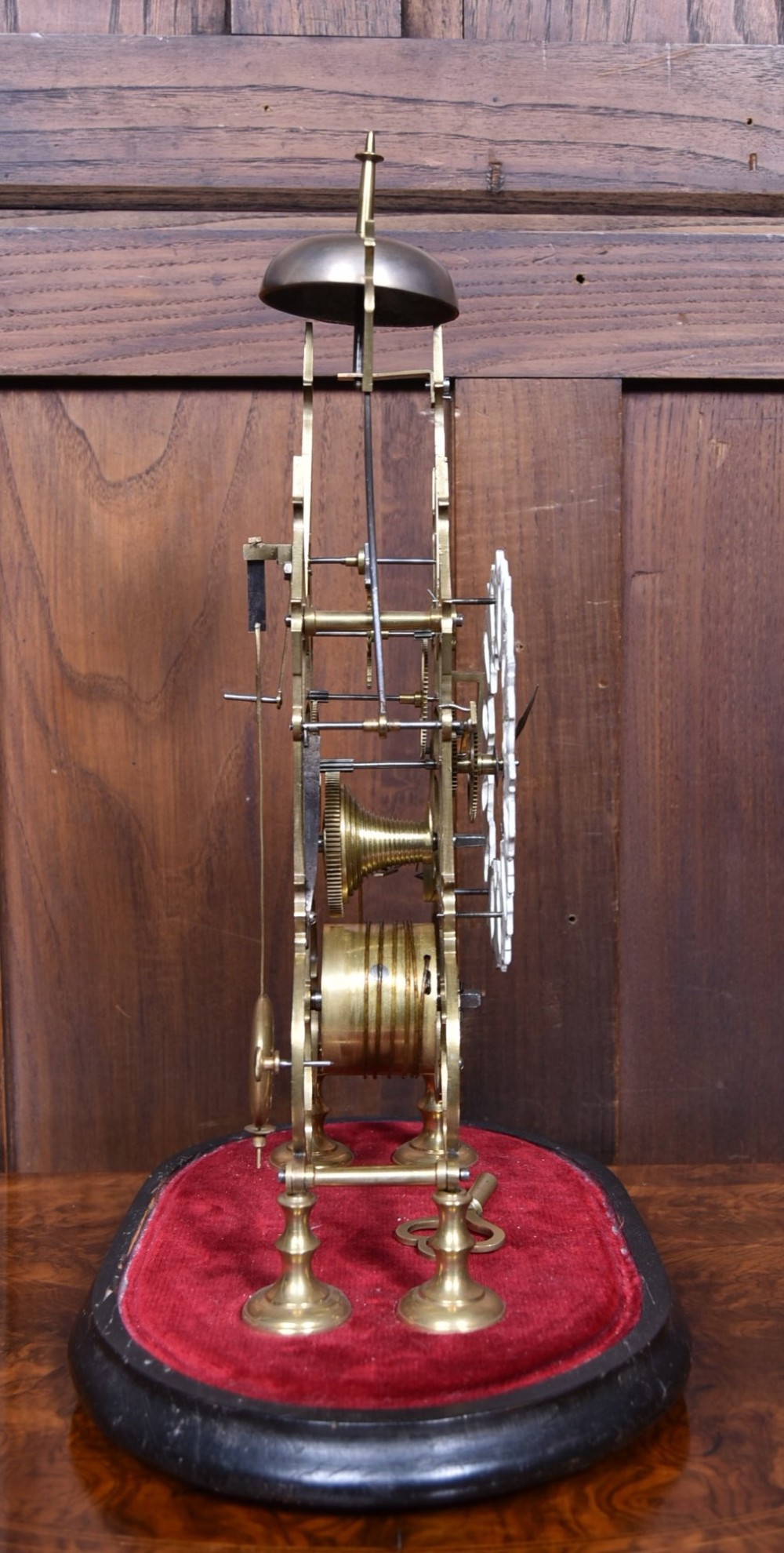 A Victorian brass skeleton clock with an openwork pierced dial and top bell, enclosed within a glass dome on an ebonised wooden base. View VI